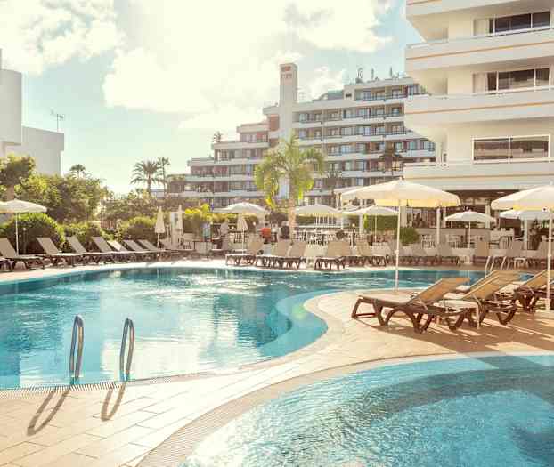 Hotellin uima-allas, aurinkotuoleja ja varjoja, ympärillä rakennuksia. (Tekoälyn luoma teksti)