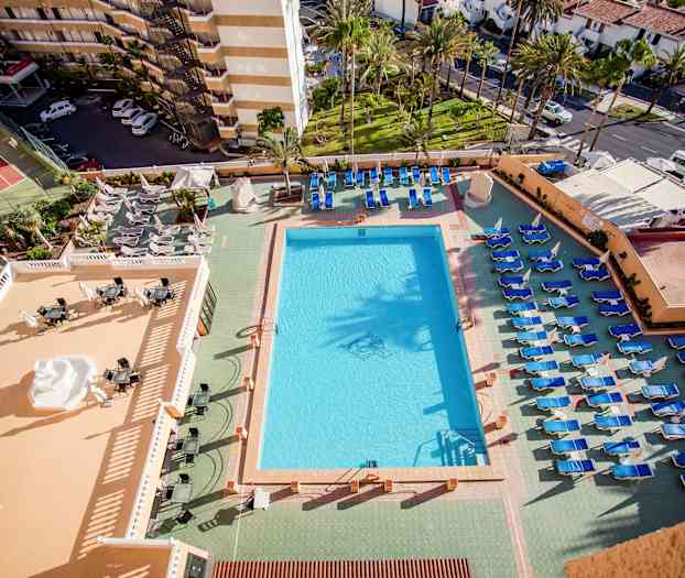 Näkymä uima-altaalle ja aurinkotuoleille hotellissa, ympärillä olevat rakennukset ja vihreät alueet näkyvät. (Tekoälyn luoma teksti)