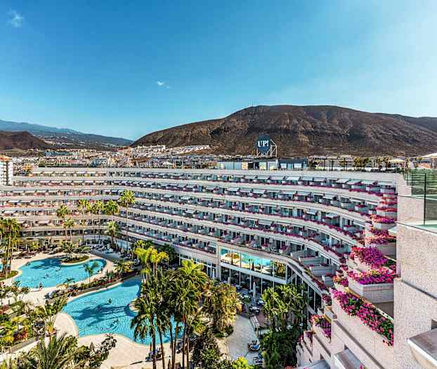 Kuva hotellikompleksista, jossa on uima-allasalue ja ympäröivä vuoristo. (Tekoälyn luoma teksti)