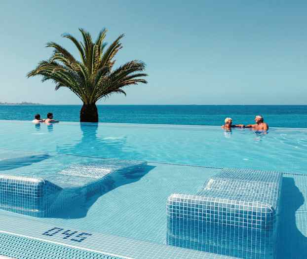 Infinity-allas, josta on näkymä merelle, keskellä palmu ja uimareita vedessä. (Tekoälyn luoma teksti)