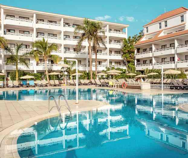 Kuva hotellikompleksista, jossa on valkoiset rakennukset, puita ja uima-allas. (Tekoälyn luoma teksti)