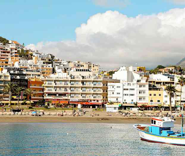 Ranta aurinkotuoleilla, kalastusvene vedessä ja rakennuksia takana. (Tekoälyn luoma teksti)