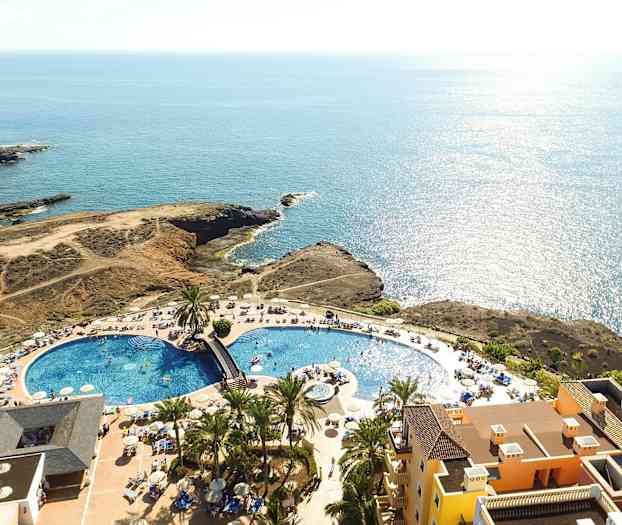 Ilmakuva lomakeskuksesta, jossa uima-allas, aurinkotuoleja ja merinäköala. (Tekoälyn luoma teksti)