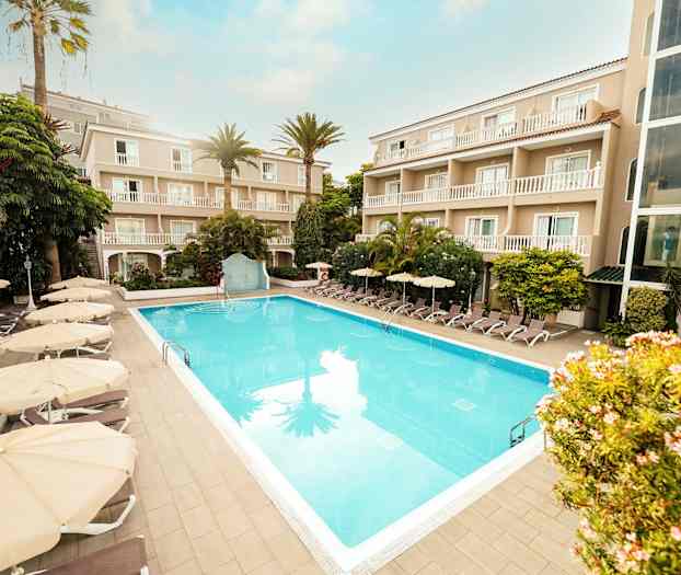 Hotellialue, jossa ulkouima-allas, ympäröity aurinkotuoleilla ja aurinkovarjoilla, sekä parvekkeellisia rakennuksia. (Tekoälyn luoma teksti)