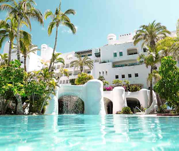 Valkoinen rakennus, jonka ympärillä on palmuja ja etualalla uima-allas. (Tekoälyn luoma teksti)