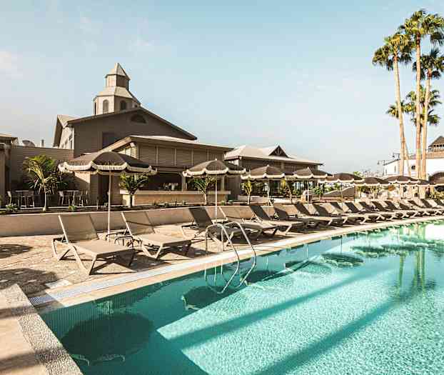 Kuva uima-allasalueesta, jossa on aurinkotuoleja, aurinkovarjoja ja rakennus taustalla. (Tekoälyn luoma teksti)