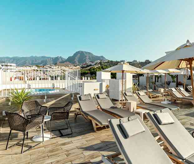Uima-allas, aurinkotuoleja ja aurinkovarjoja hotelliterassilla, taustalla vuoria. (Tekoälyn luoma teksti)