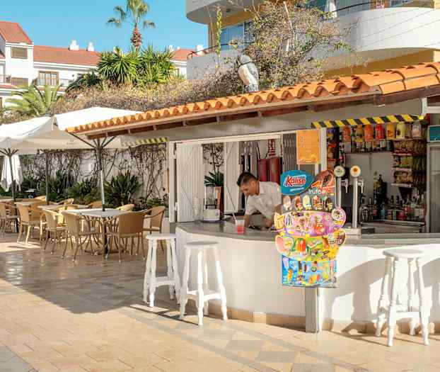 Ulkoilmaravintola, jossa pöytiä ja varjoja baarin vieressä. (Tekoälyn luoma teksti)