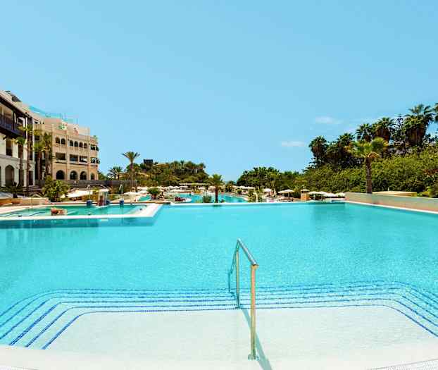 Suuri uima-allas hotellin vieressä, ympärillä vihreää kasvillisuutta. (Tekoälyn luoma teksti)