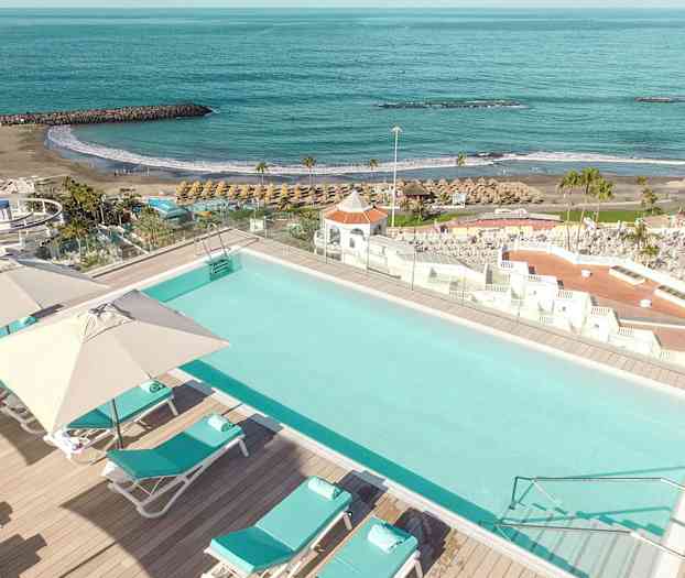 Uima-allas aurinkotuoleilla ja varjoilla, jotka sijaitsevat lähellä rantaa ja merta. (Tekoälyn luoma teksti)