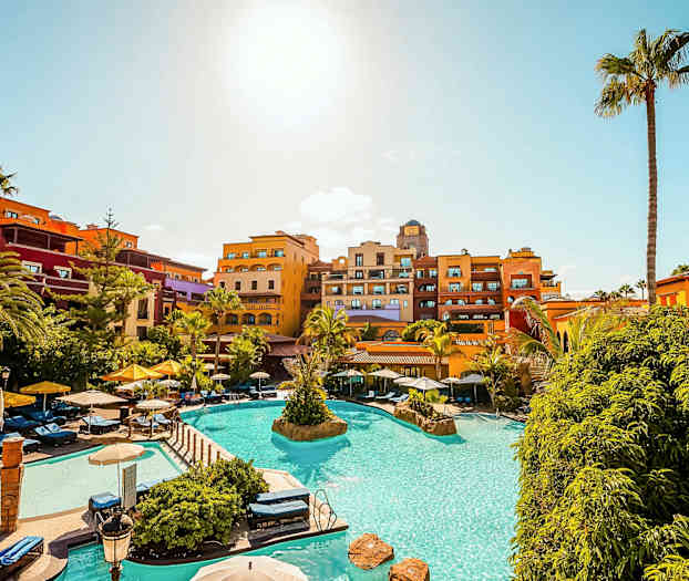 Lomakohde uima-altaalla, aurinkotuoleilla ja värikkäillä hotellirakennuksilla kirkkaan sinisen taivaan alla. (Tekoälyn luoma teksti)