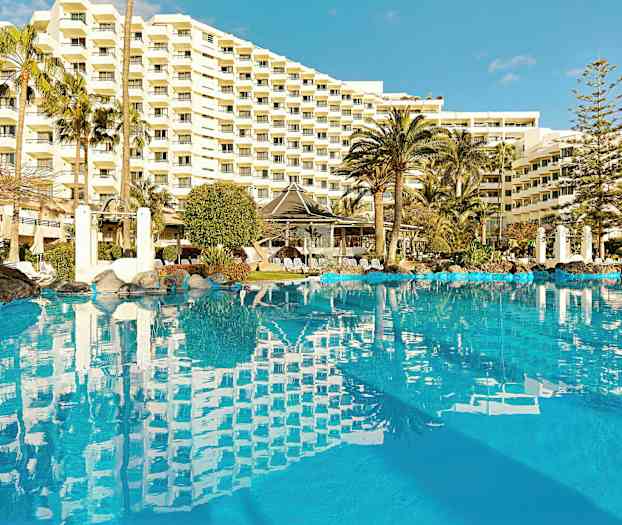 Kuva ulkouima-altaasta, jonka ympärillä on palmuja ja taustalla suuri hotelli. (Tekoälyn luoma teksti)