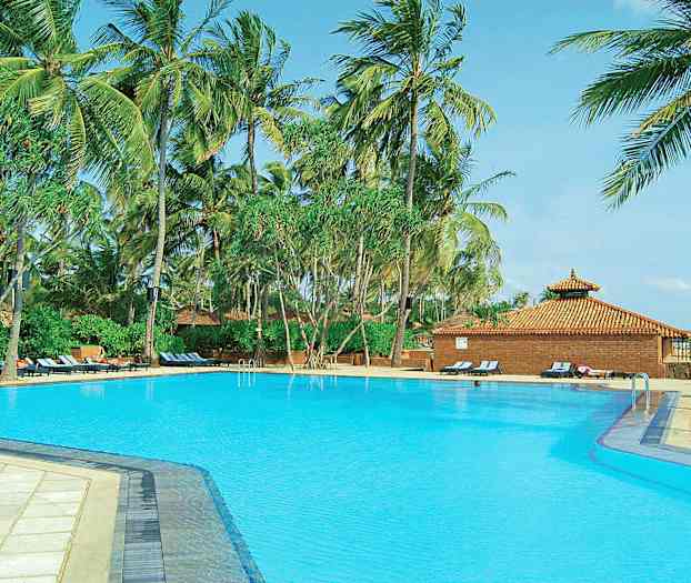 Iso uima-allas, jota ympäröivät korkeat palmut ja aurinkotuolit lähellä tiilikattoista rakennusta. (Tekoälyn luoma teksti)