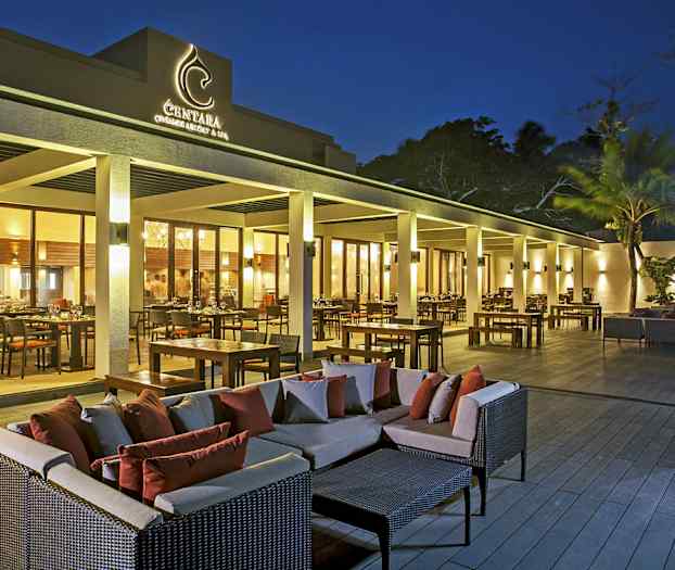 Ulkoterassi ravintolan edustalla, jossa on pöytiä, tuoleja ja sohvia hämärässä valaistuksessa. (Tekoälyn luoma teksti)