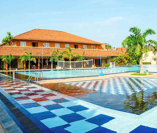 Suuri ulkouima-allas, jossa värikäs laatoitettu alue, ympärillä palmuja ja tiilenvärisiä rakennuksia. (Tekoälyn luoma teksti)