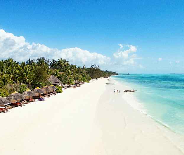 Ranta, jossa on valkoista hiekkaa ja kirkasta sinistä vettä, ympäröitynä vehmailla palmuilla ja aurinkovarjotuoleilla. (Tekoälyn luoma teksti)