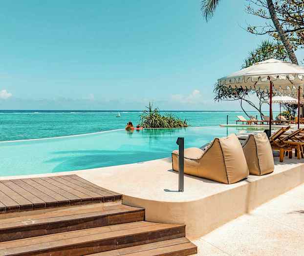 Infiniteettiuima-allas meren äärellä, ympäröity aurinkotuoleilla ja varjoilla. (Tekoälyn luoma teksti)