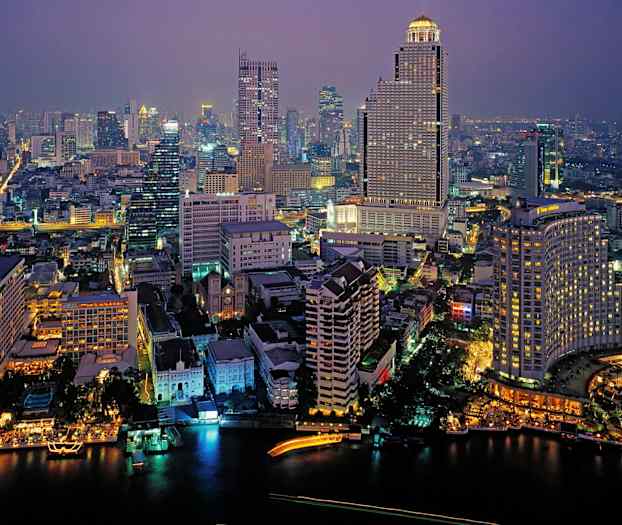 Kaupunkinäkymä illalla, jossa valoja on rakennuksissa ja kaduilla, ja etualalla virtaa joki. (Tekoälyn luoma teksti)