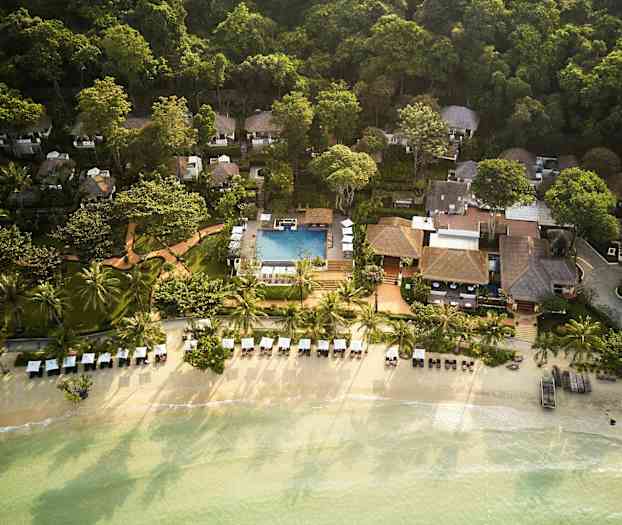 Ilmakuva lomakeskuksesta rannalla, jossa on palmuja, aurinkotuoleja ja uima-allas rehevän vehreyden keskellä. (Tekoälyn luoma teksti)