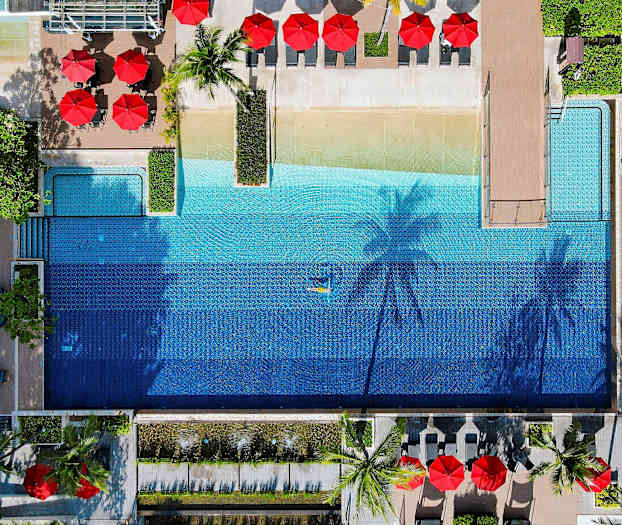 Ilmakuva ulkouima-altaasta, jota ympäröivät aurinkotuolit ja aurinkovarjot. (Tekoälyn luoma teksti)