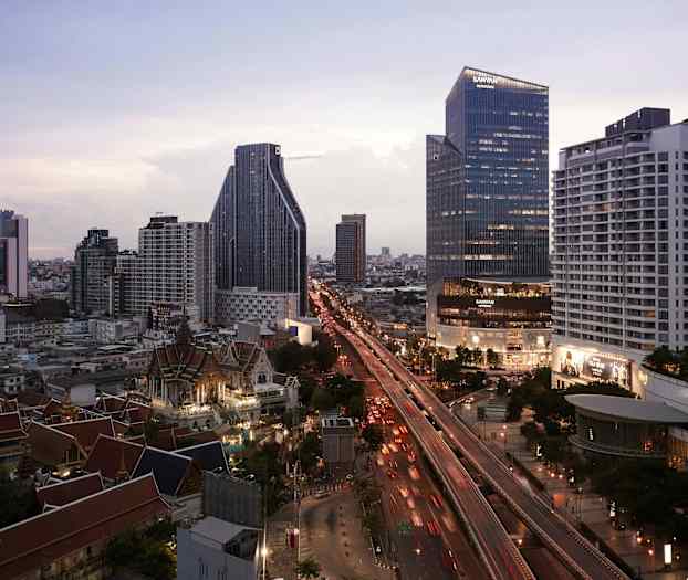 Kaupungin siluetti, jossa näkyy moderneja korkeita rakennuksia, vilkas tie ja perinteisiä rakennuksia etualalla. (Tekoälyn luoma teksti)