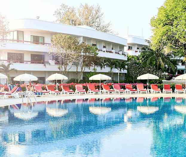 Uima-allasalue, jossa aurinkotuoleja ja varjoja hotellin edessä. (Tekoälyn luoma teksti)