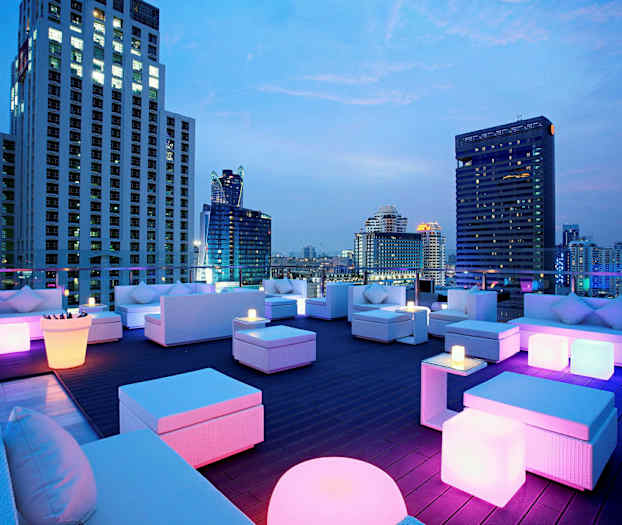 Katoterassi modernilla kalusteilla ja värikkäällä valaistuksella, ympärillä korkeita rakennuksia illalla. (Tekoälyn luoma teksti)