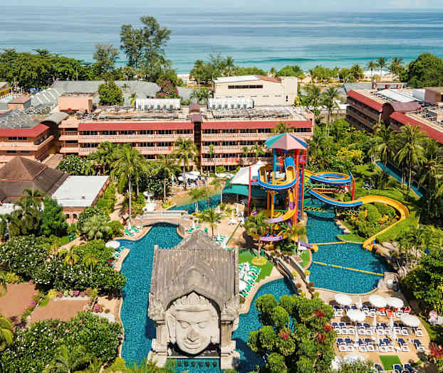 Ulkotila, jossa on vesipuisto, uima-allas ja viheralueita rakennusten edustalla lähellä merta. (Tekoälyn luoma teksti)