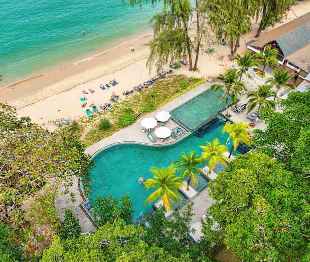 Ilmakuva rannasta, jossa on aurinkotuoleja ja uima-allasalue vehreyden keskellä. (Tekoälyn luoma teksti)