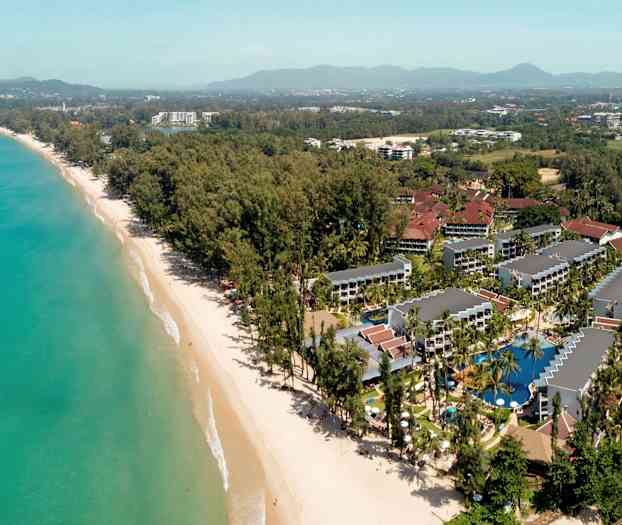 Ilmakuva lomakeskuksesta rannalla, ympärillä puita ja rakennuksia. (Tekoälyn luoma teksti)