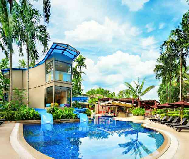 Moderni rakennus, jota ympäröivät palmut ja aurinkotuolit uima-altaan äärellä. (Tekoälyn luoma teksti)