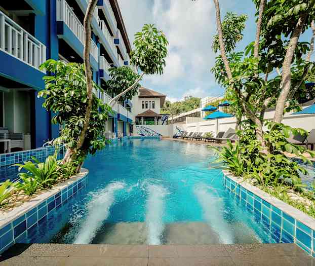 Uima-allas, jota ympäröivät vehreät kasvit, rakennus ja aurinkotuolit. (Tekoälyn luoma teksti)