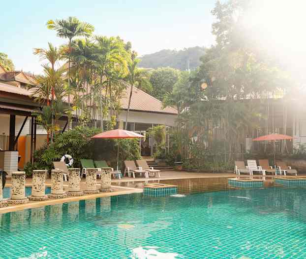 Ulkouima-allas, jolla on aurinkotuoleja ja aurinkovarjoja, vehreiden puiden ympäröimänä. (Tekoälyn luoma teksti)