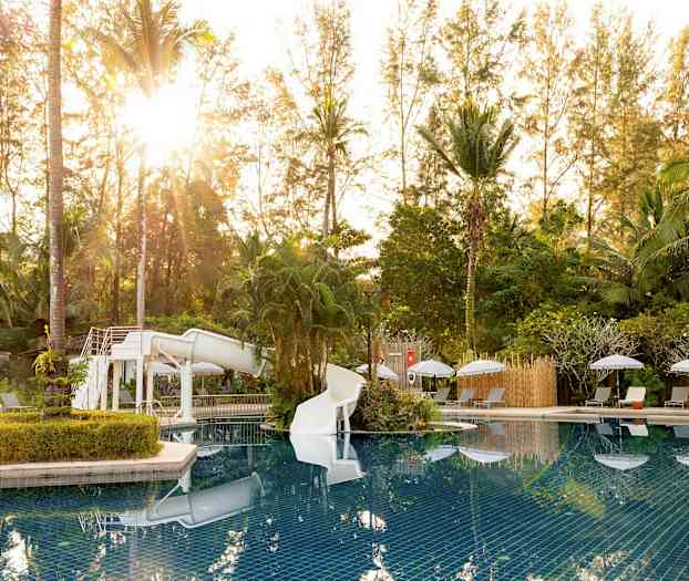 Uima-allasalue vesiliukumäellä, jota ympäröivät aurinkotuolit ja vehreys. (Tekoälyn luoma teksti)