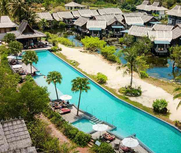 Useita viehättäviä bungaloweja uima-altaan reunalla, jossa aurinkotuoleja ja aurinkovarjoja, vehreyden ympäröimänä. (Tekoälyn luoma teksti)