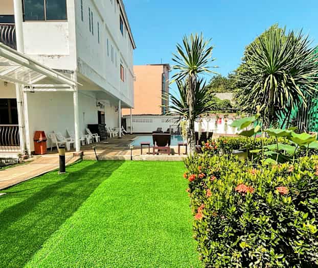 Ulkoilma kuva rakennuksesta, jossa on vihreä nurmikko ja ympäröiviä kasveja. (Tekoälyn luoma teksti)