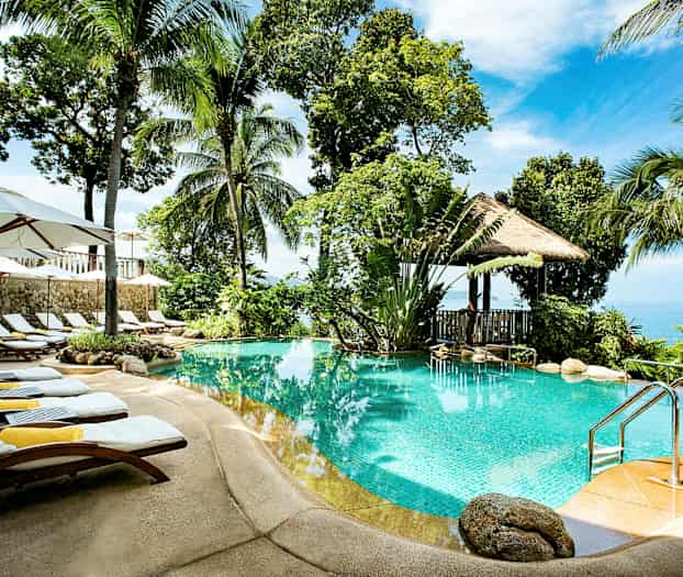 Ulkouima-allas, jota ympäröivät palmut, aurinkotuolit ja aurinkovarjot, taustalla näkymä merelle. (Tekoälyn luoma teksti)