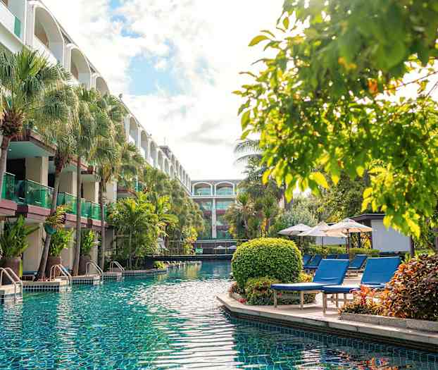 Uima-allas, jossa kirkasta vettä, ympäröitynä aurinkotuoleilla, aurinkovarjoilla ja vehreillä puilla, lähellä rakennusta parvekkeineen. (Tekoälyn luoma teksti)