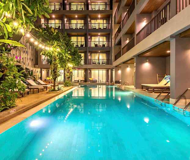 Ulkoallas, jota ympäröivät aurinkotuolit ja vehreä kasvillisuus modernin hotellin edessä. (Tekoälyn luoma teksti)