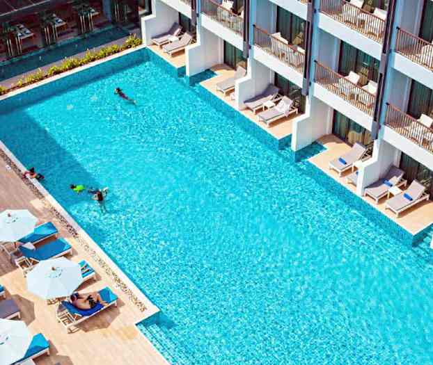 Ulkouima-allas, jossa aurinkotuoleja ja varjoja reunalla sekä rakennuksia terasseineen. (Tekoälyn luoma teksti)