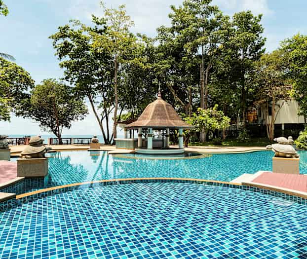 Uima-allas hotellialueella, jota ympäröivät puut, pieni paviljonkia muistuttava katos ja reunaa koristavat kilpikonna-aiheiset koristeet. (Tekoälyn luoma teksti)