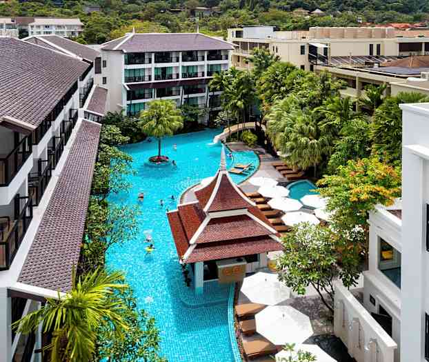 Valoisa kuva hotellialueesta, jossa on suuri uima-allas ja ympärillä vihreitä puita ja rakennuksia ruskeine kattoineen. (Tekoälyn luoma teksti)