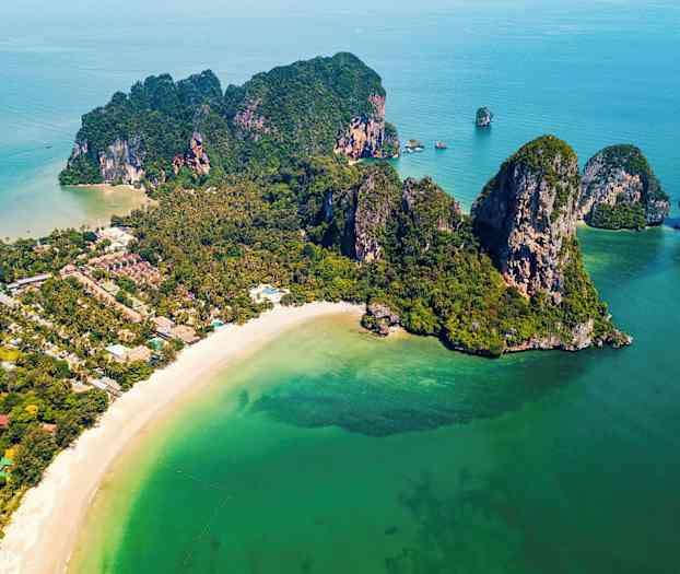 Ilmakuva rannasta, jossa on hiekkaranta, vihreitä kallioita ja kasvillisuutta sekä kirkasta turkoosia vettä. (Tekoälyn luoma teksti)