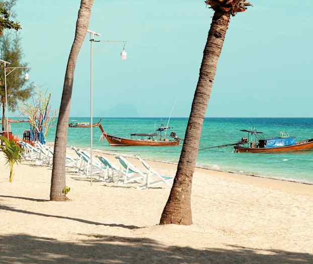 Ranta, jossa palmuja, aurinkotuoleja ja perinteisiä puuveneitä meressä. (Tekoälyn luoma teksti)