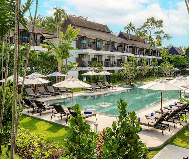 Kuva hotellin uima-altaasta, jonka ympärillä on aurinkotuoleja ja aurinkovarjoja, taustalla vehreä puutarha ja hotelli. (Tekoälyn luoma teksti)