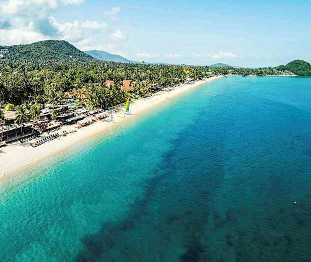 Hiekkaranta, jossa turkoosia merta, ympäröitynä puilla ja taloilla, ihmiset rentoutuvat. (Tekoälyn luoma teksti)