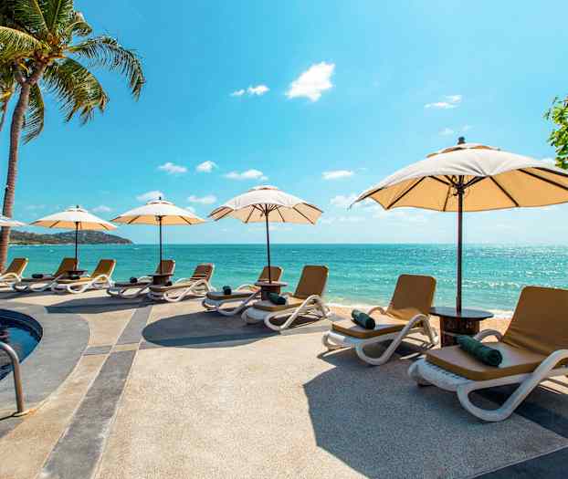 Ranta, jossa aurinkotuoleja ja aurinkovarjoja altaan vieressä lähellä merta. (Tekoälyn luoma teksti)