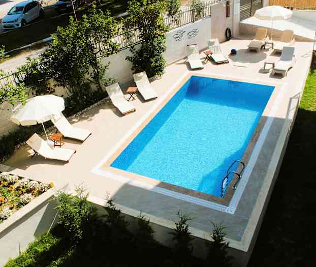 Suorakulmainen uima-allas, jonka vieressä aurinkotuoleja ja aurinkovarjoja. (Tekoälyn luoma teksti)