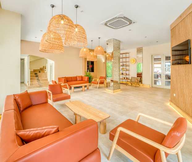 Vaalea oleskelutila, jossa on ruskeat sohvat ja nojatuolit, puupöydät ja roikkuvat rottinkivalaisimet. (Tekoälyn luoma teksti)