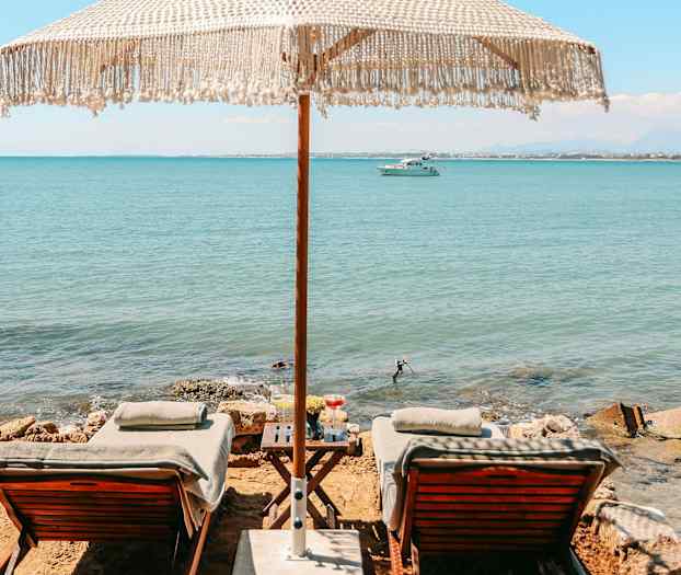 Kaksi aurinkotuolia ja varjo meren rannalla. (Tekoälyn luoma teksti)